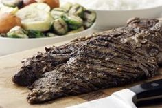 a piece of meat sitting on top of a cutting board next to a bowl of vegetables