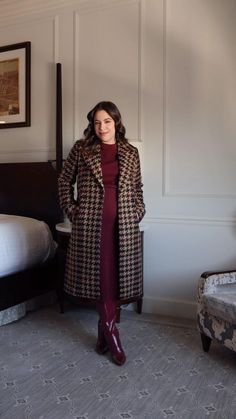 a woman standing in front of a bed wearing a long coat and red dress with boots