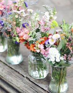 four glass vases filled with colorful flowers on top of a wooden table next to each other