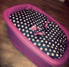 a pink and black polka dot baby bed with purple trim on the bottom, in front of a wooden floor