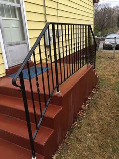 a set of stairs leading up to a yellow house with a black hand rail on it