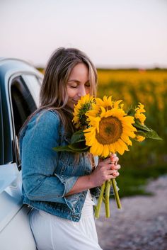 a woman holding a bouquet of sunflowers in front of a car on the road