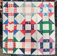 a person holding up a quilt made with different colored blocks and shapes on it's sides