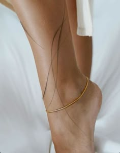 a woman's foot with a gold bracelet on top of her ankles and the bottom part of her leg