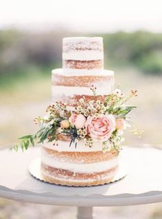 a three tiered cake with flowers and greenery sits on top of a table