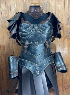 a woman's leather armor on display in front of a wooden wall with metal straps