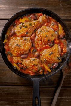 a skillet filled with chicken and beans on top of a wooden table next to a spoon