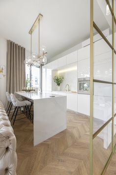 an open kitchen and living room area in a modern apartment with white walls, wood flooring and gold accents