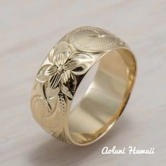 a gold wedding ring with an engraved flower on the front and side, sitting on a white surface