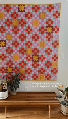 a table with two potted plants and a large quilt on the wall behind it