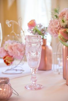 there is a glass on the table with flowers in vases and candles behind it