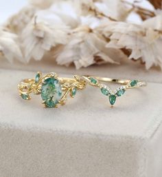 two gold rings with green and white stones on top of each other next to dried flowers