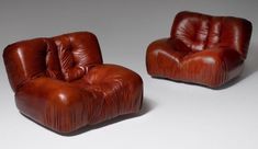 two brown leather chairs sitting next to each other on a white surface with no one in it