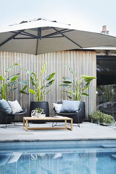 an umbrella over a pool with two chairs and a coffee table in front of it