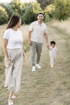 a man and woman holding hands walking down a path with a small child on the other side