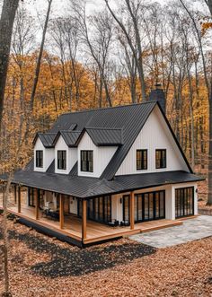 a white house in the woods surrounded by trees with leaves on the ground and fallen leaves all around it