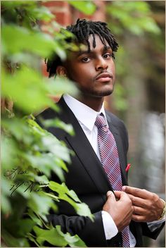 a man with dreadlocks wearing a suit and tie standing in front of trees