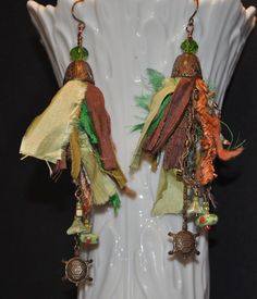 These light-weight tassel earrings have so much detail and variety that they will match with a variety of outfits. The colors range from green, light green, mustard, and brown to name a few.  They have a drop length of 4.75 inches. The ear wires are hand made from fired copper which gives them a beautiful color and strength. I also include plastic safety backs so they won't accidentally fall out. A wide variety of tassels hang from an ornate antiqued brass bead cap.  Some of the materials used in the tassels include but aren't limited to: recycled sari silk, ribbon, yarn, up-cycled cotton, threaded seed beads, and petite antiqued brass chain.  There are three lengths of chain in each earring from which the intricate antiqued brass turtles hang, along with assorted seed beads and a delicate Green Tassel Earrings With Fringe For Festivals, Green Tassel Earrings With Latkans For Gifts, Bohemian Green Tassel Earrings For Festivals, Green Fringe Earrings For Festival, Green Tassel Dangle Earrings, Green Dangle Tassel Earrings For Festival, Green Beaded Tassel Drop Earrings, Green Dangle Tassel Earrings For Pierced Ears, Green Dangle Tassel Earrings With Latkans