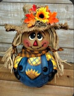 a scarecrow doll with an orange flower on her head and blue overalls, sitting on a wooden surface