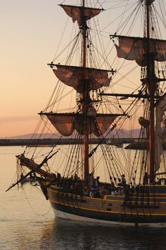 an old sailing ship in the water with people on it's deck at sunset