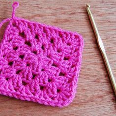 a crochet square is sitting on a table next to a knitting needle