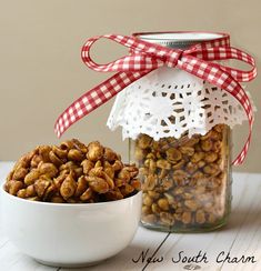 a jar filled with nuts sitting next to a white bowl full of nuts on top of a table