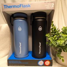 two thermoflask water bottles are sitting next to a potted plant