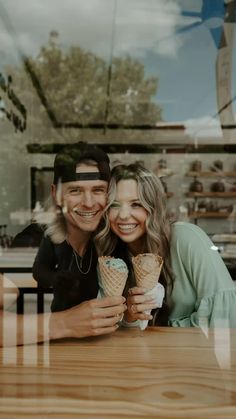 a man and woman sitting at a table with an ice cream cone in their hands