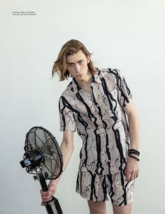 a young man holding a fan and posing for a photo in front of a white wall