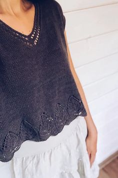 a woman standing in front of a white wall wearing a black knitted top with crochet details