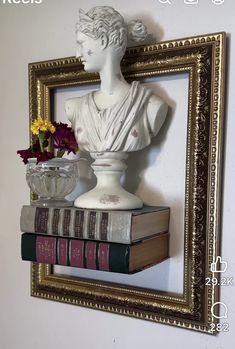 a white busturine sitting on top of a pile of books next to a vase filled with flowers