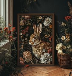 a painting of a rabbit surrounded by flowers in a wooden frame on the floor next to a window