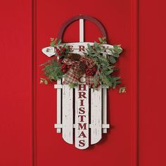 a red door with a christmas sign hanging on it's side and greenery