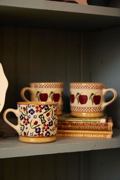 three coffee cups are sitting on a shelf next to two books and a teapot