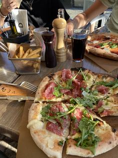 two pizzas sitting on top of a wooden table next to glasses of soda and silverware