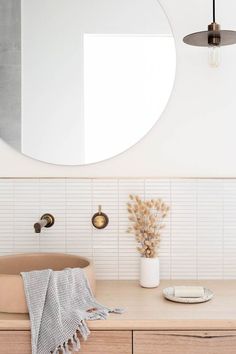 a bathroom sink with a round mirror above it next to a wooden cabinet and light fixture