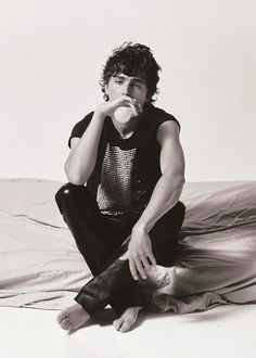 a young man sitting on top of a bed drinking from a glass in his mouth