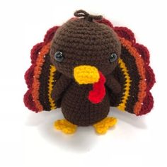 a crocheted turkey stuffed animal with a red tail and black eyes sits in front of a white background