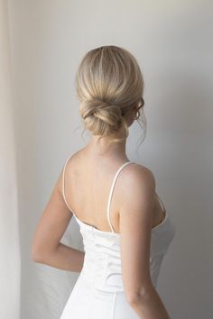 a woman in a white dress is looking down at her hair and wearing an updo