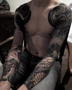 a man sitting in a chair with tattoos on his arm and chest, looking at the camera