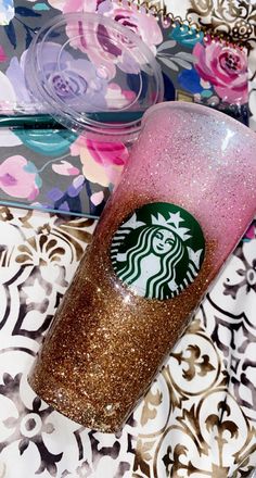 a starbucks cup sitting on top of a table next to a flowery wallpaper