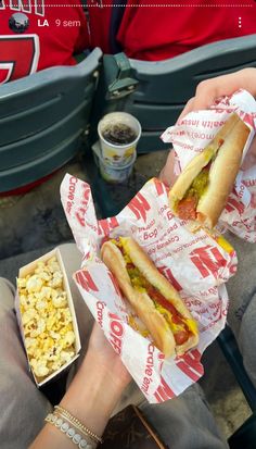 two people eating hot dogs and popcorn at a sporting event