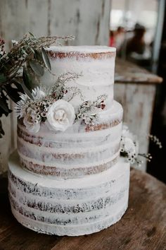 a three tiered cake with flowers and greenery sits on top of a wooden table