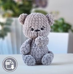 a crocheted teddy bear sitting on top of a table next to a potted plant