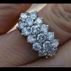 a woman's hand holding a ring with several diamonds on it and the center diamond is surrounded by smaller round stones