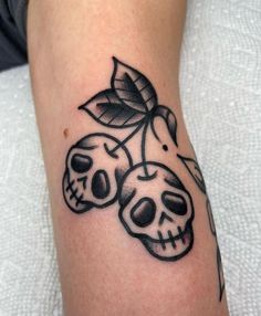 a skull and two cherries tattoo on the left arm, with leaves growing out of it