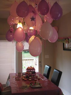 a party table with pink and white balloons hanging from the ceiling