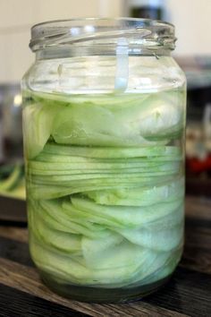 a glass jar filled with sliced green onions on top of a wooden table next to a knife