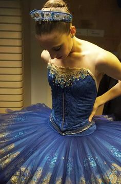 a woman in a blue and gold dress with her hands on her hips while wearing a tiara