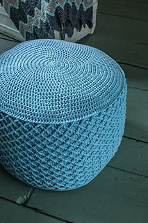 a blue knitted ottoman sitting on top of a wooden floor next to a rug